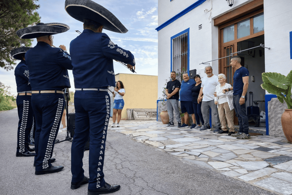 Mariachi Reyes De México ofreciendo serenata a domicilio frente a una vivienda con trajes charros azul marino interpretando música con trompeta, violín y guitarras para una familia.